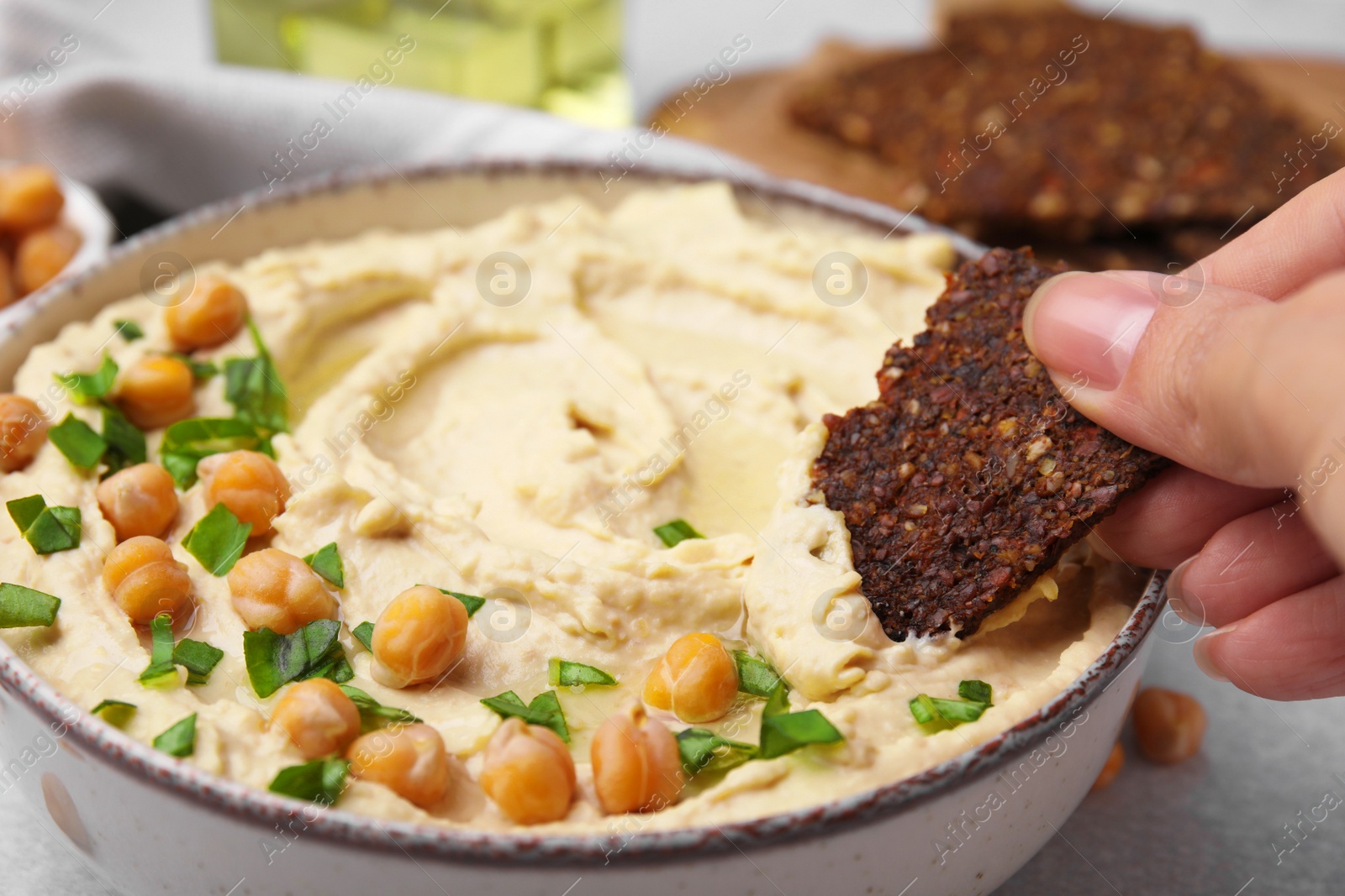 Photo of Woman taking delicious hummus with crispbread at grey table, closeup