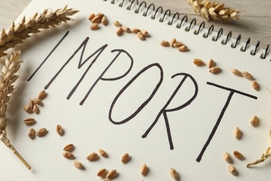 Notebook with word import and ears of wheat on table, closeup