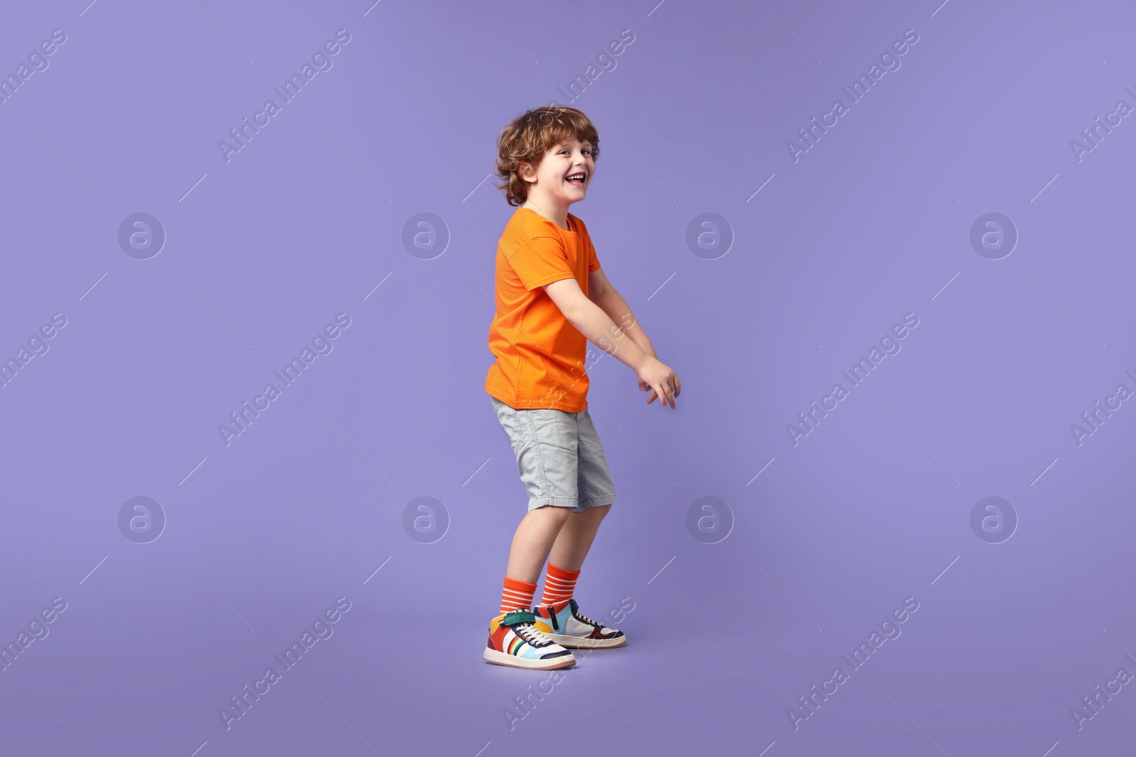 Photo of Happy little boy dancing on violet background