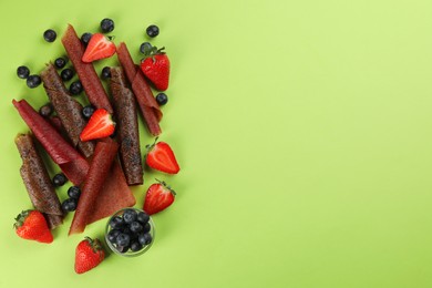 Delicious fruit leather rolls and berries on green background, flat lay. Space for text