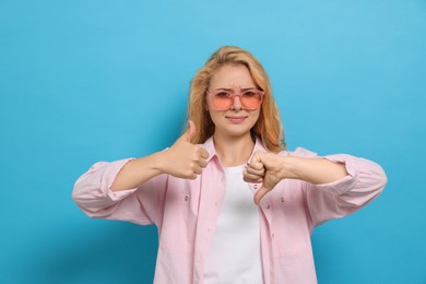 Conflicted young woman showing thumbs up and down gestures on light blue background