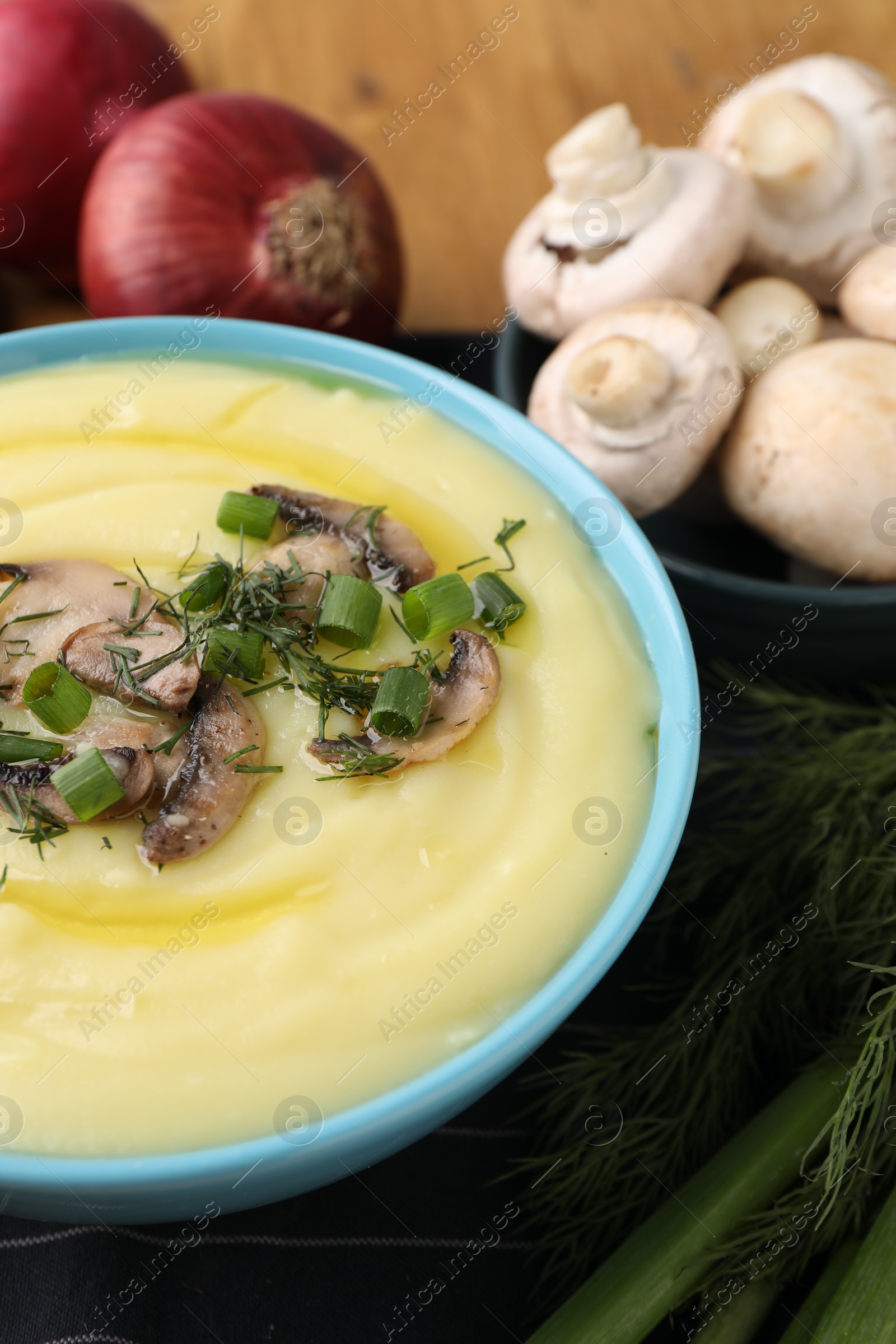 Photo of Bowl of tasty cream soup with mushrooms, green onions and dill on table, closeup