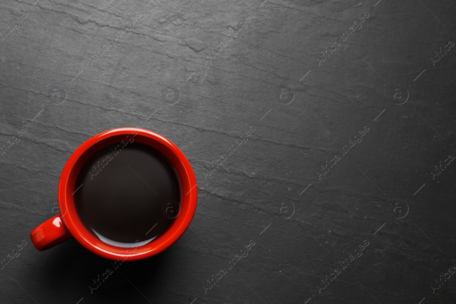 Photo of Red cup with aromatic coffee on black textured table, top view. Space for text