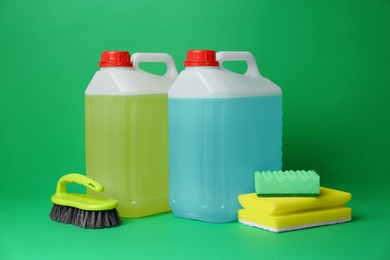 Photo of Canisters of detergents and tools on green background. Cleaning supplies