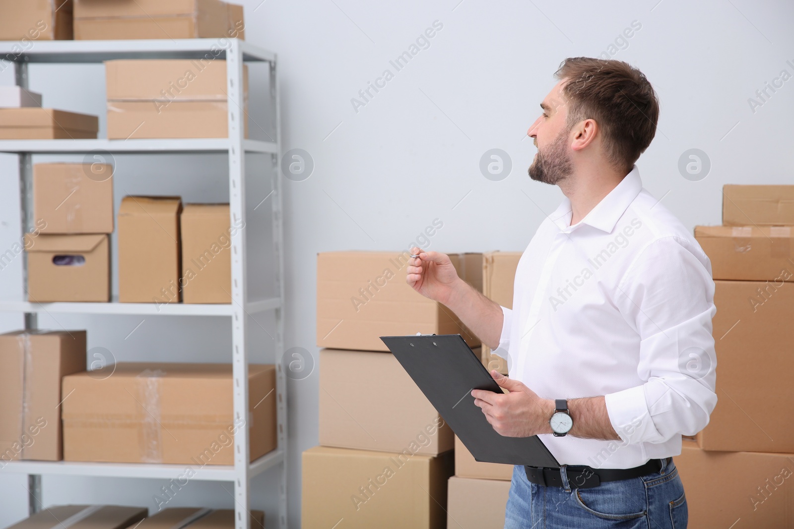 Photo of Young businessman with clipboard near cardboard boxes at warehouse