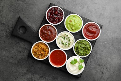 Different tasty sauces in bowls on grey table, top view