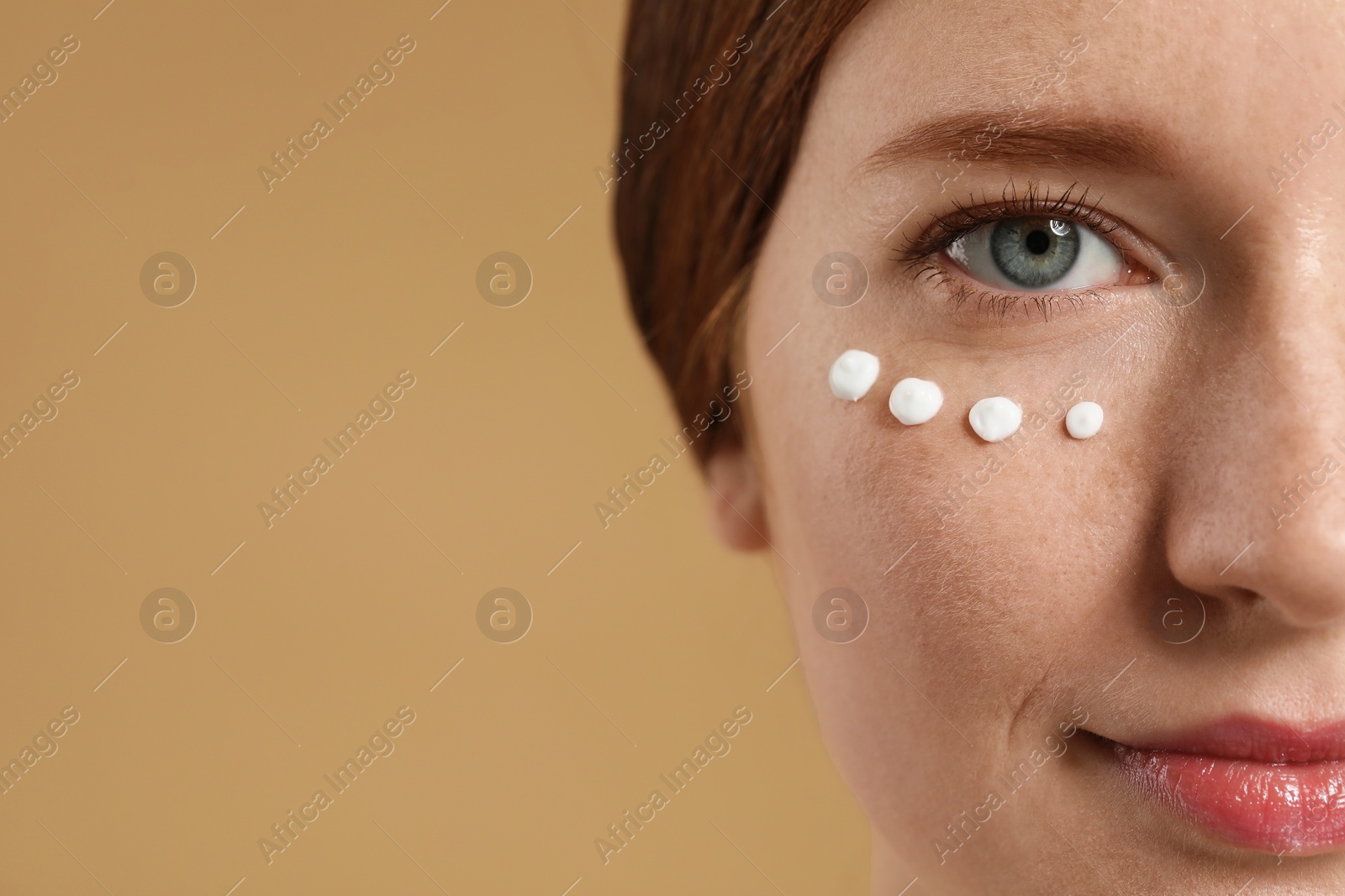 Photo of Beautiful woman with freckles and cream on her face against beige background, closeup. Space for text