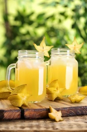 Delicious carambola juice and fresh fruits on wooden table against blurred background