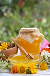 Photo of Delicious honey, combs and different flowers on white wooden table in garden