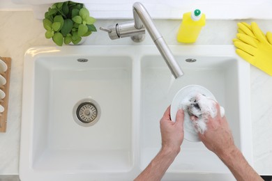 Man washing plate in kitchen sink, top view