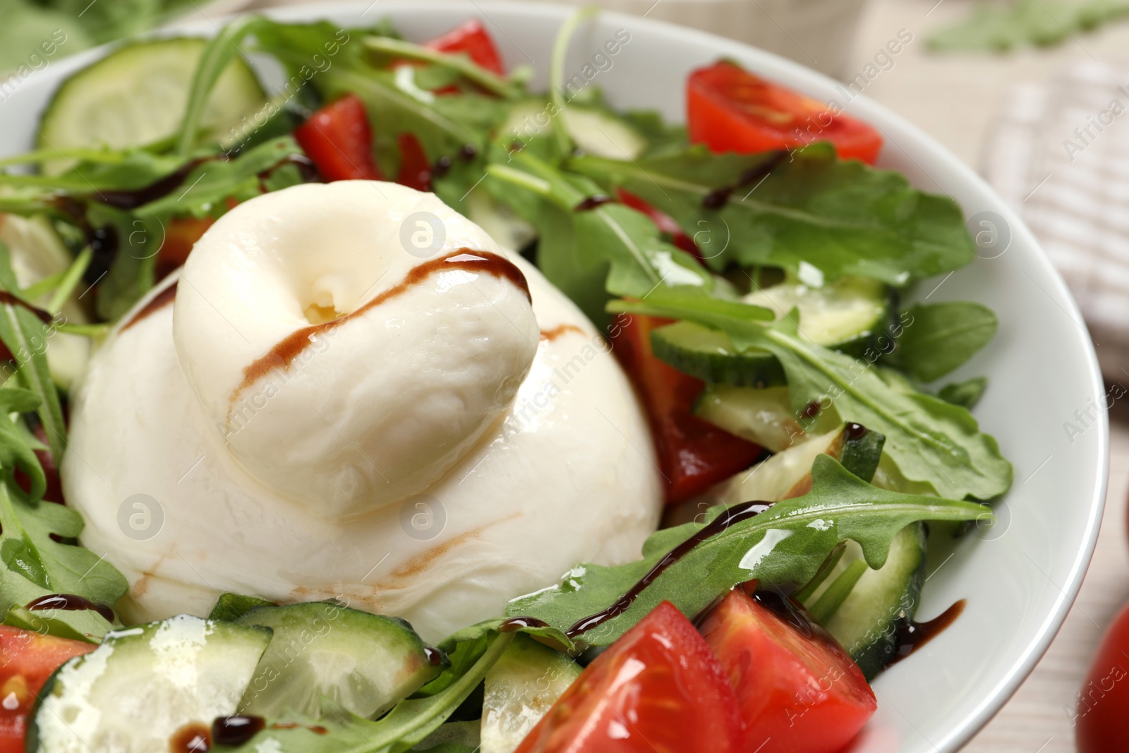 Photo of Delicious burrata salad with arugula, tomatoes and cucumbers, closeup