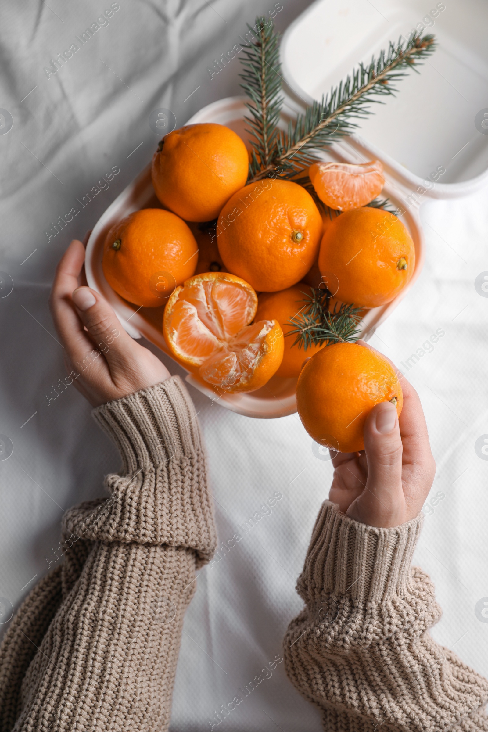 Photo of Woman with delicious ripe tangerines on white bedsheet, top view