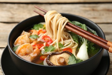 Bowl of delicious ramen with chopsticks on table, closeup. Noodle soup