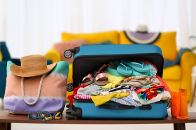 Photo of Open suitcase with different beach clothes and accessories on table