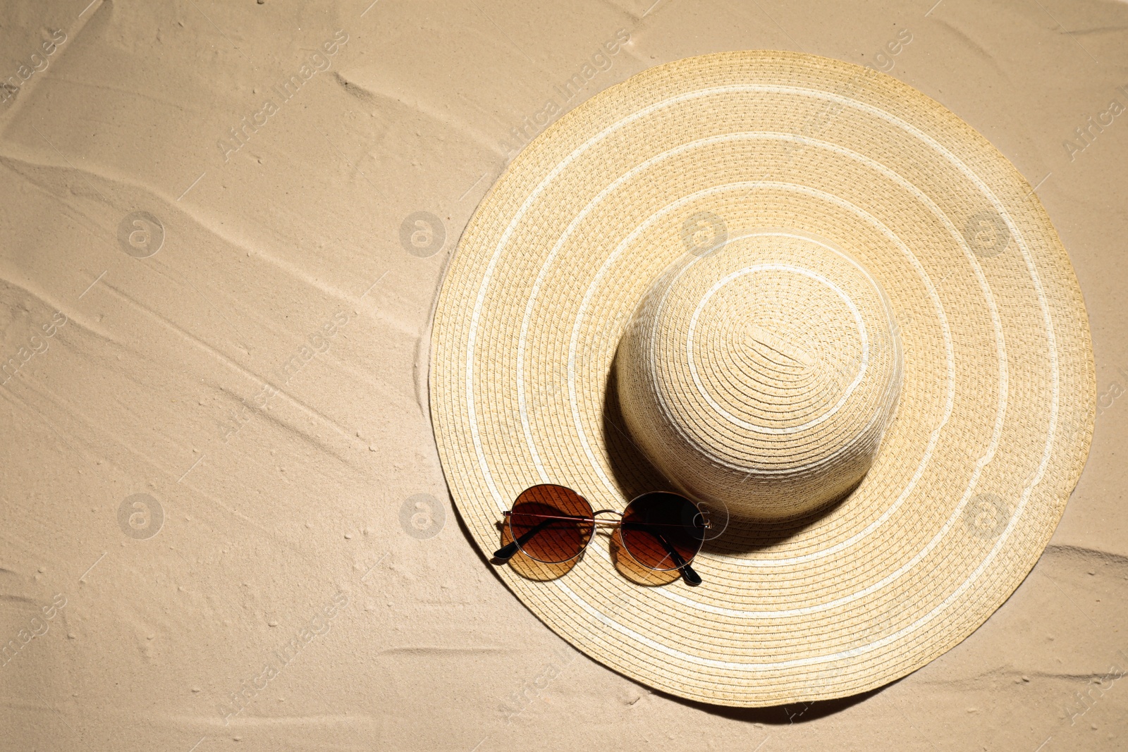 Photo of Hat and sunglasses on sand, top view. Beach accessories