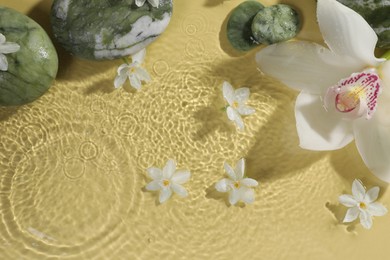 Beautiful flowers and spa stones in water on pale yellow background, top view