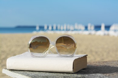 Photo of Book and sunglasses on table at seaside, space for text