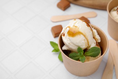 Photo of Scoopsice cream with caramel sauce, mint leaves and candies on white tiled table, closeup. Space for text