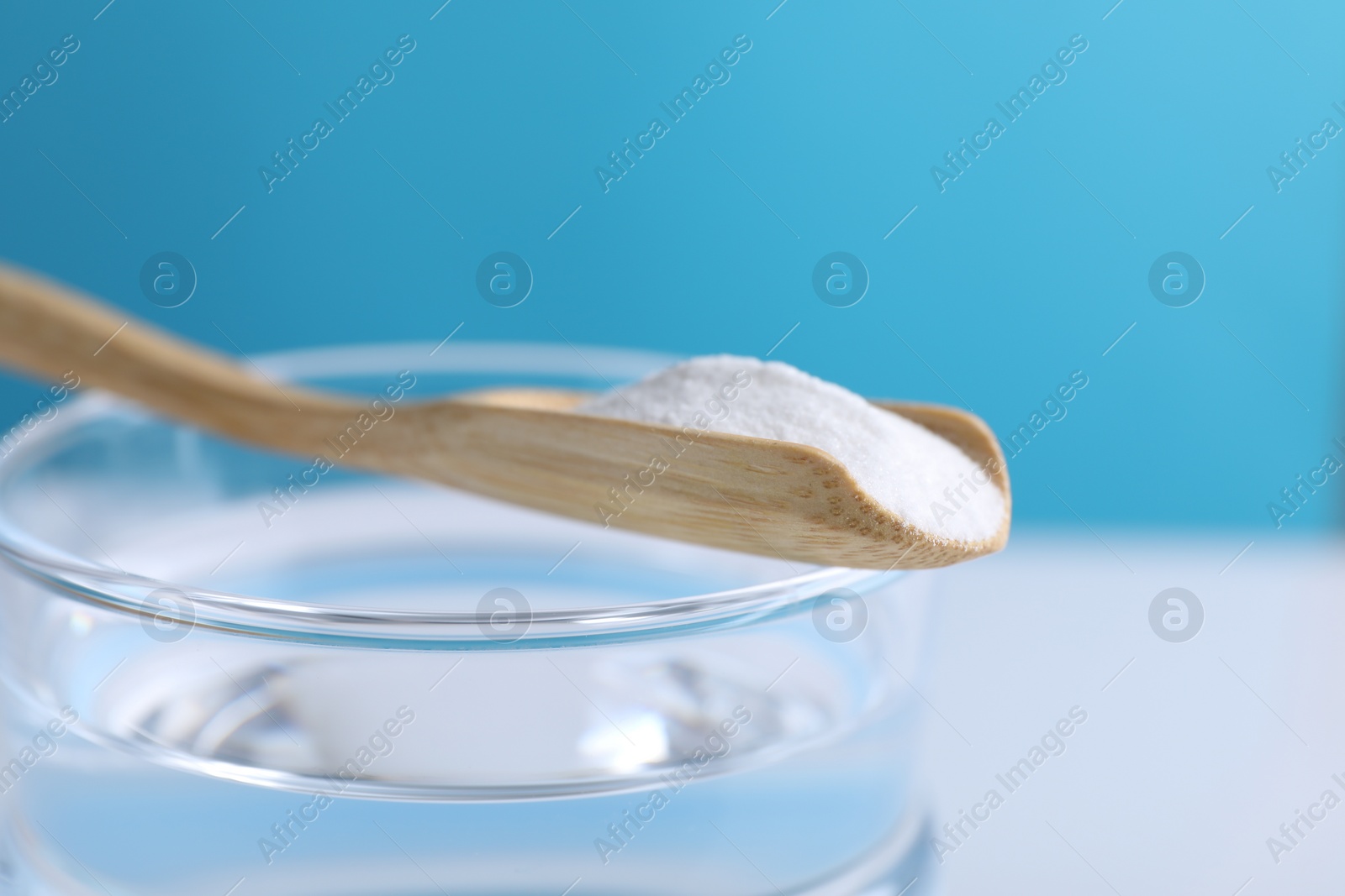 Photo of Glass of water and spoon with baking soda on color background, closeup