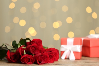 Photo of Beautiful red roses and gift boxes on table against blurred lights, space for text. St. Valentine's day celebration
