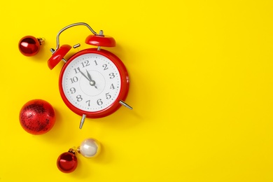 Photo of Alarm clock and festive decor on yellow background, flat lay with space for text. New Year countdown