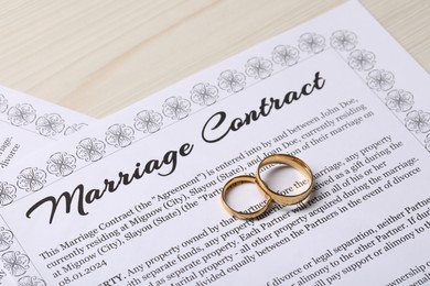 Marriage contracts and gold rings on light wooden table, closeup