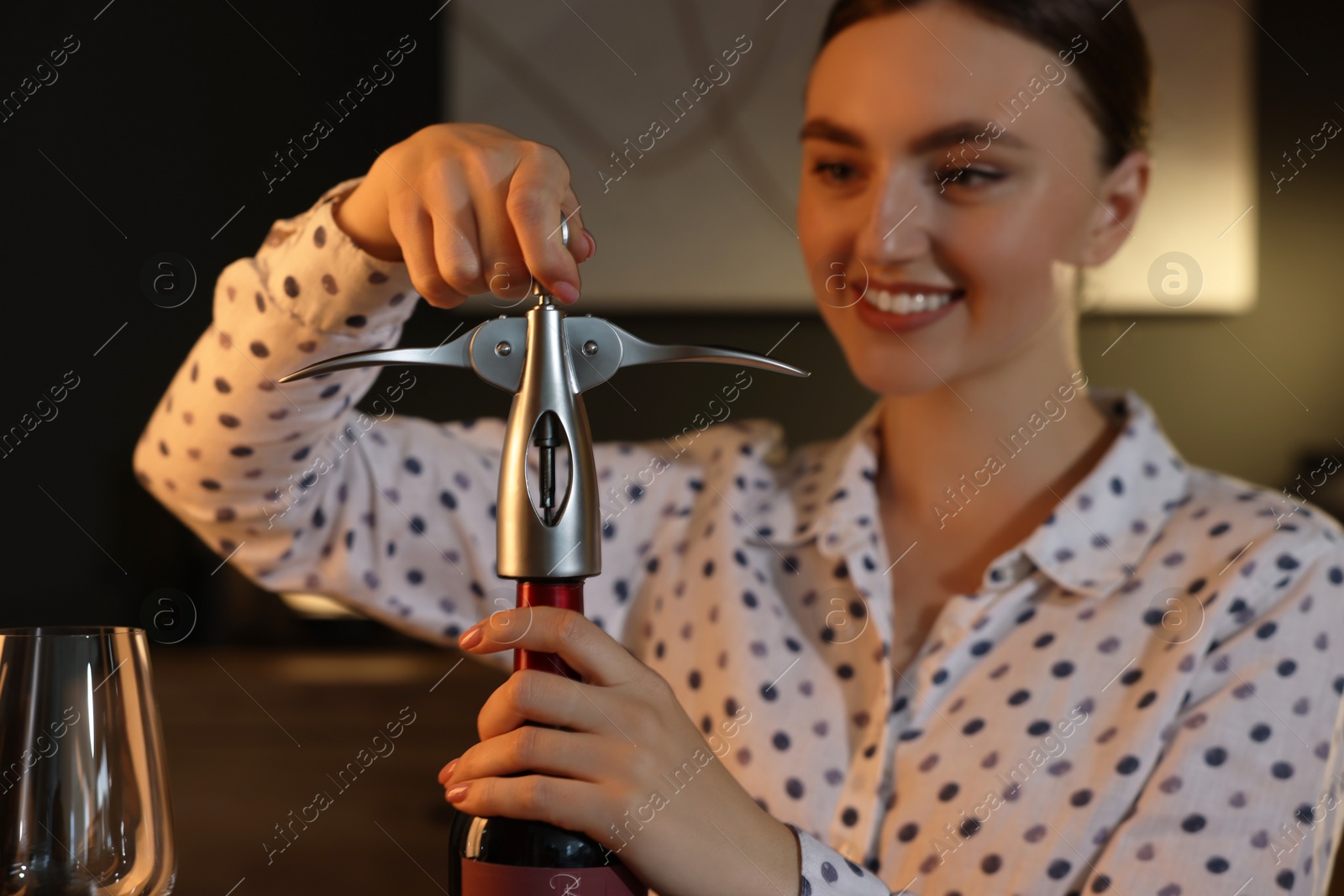 Photo of Romantic dinner. Woman opening wine bottle with corkscrew indoors, selective focus