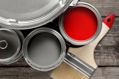 Photo of Cans of paints and brush on wooden table, flat lay