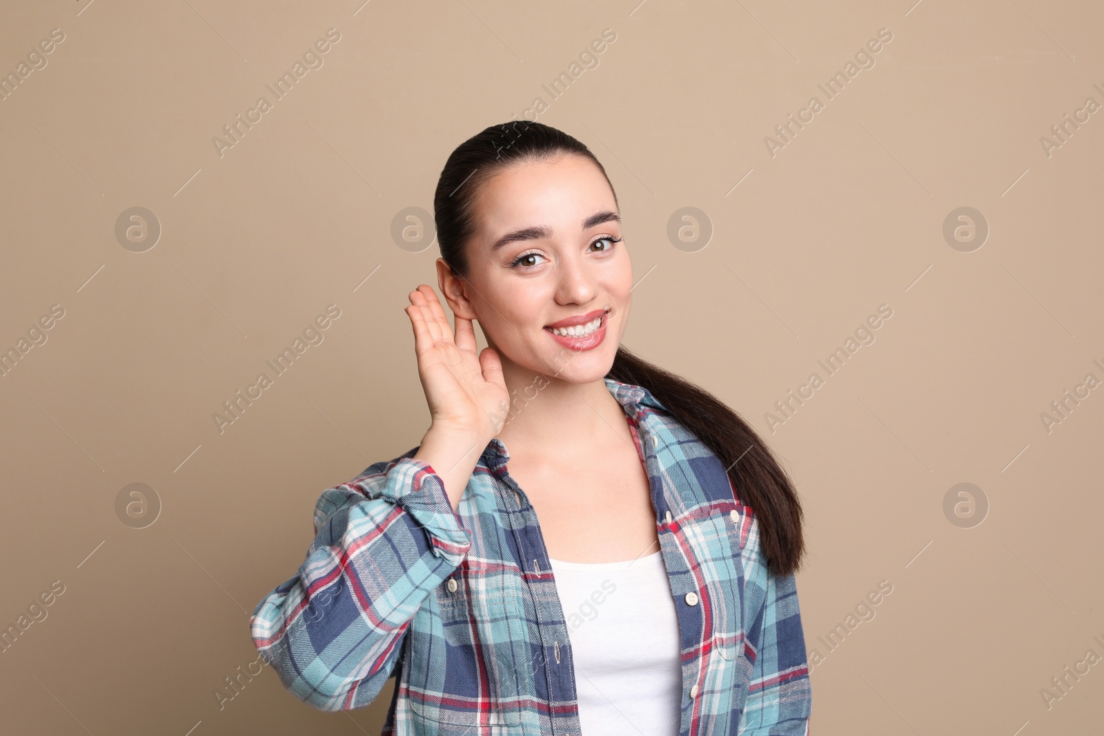 Photo of Young woman showing hand to ear gesture on beige background