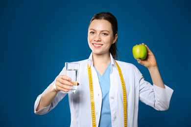 Photo of Nutritionist with glass of water and apple on blue background