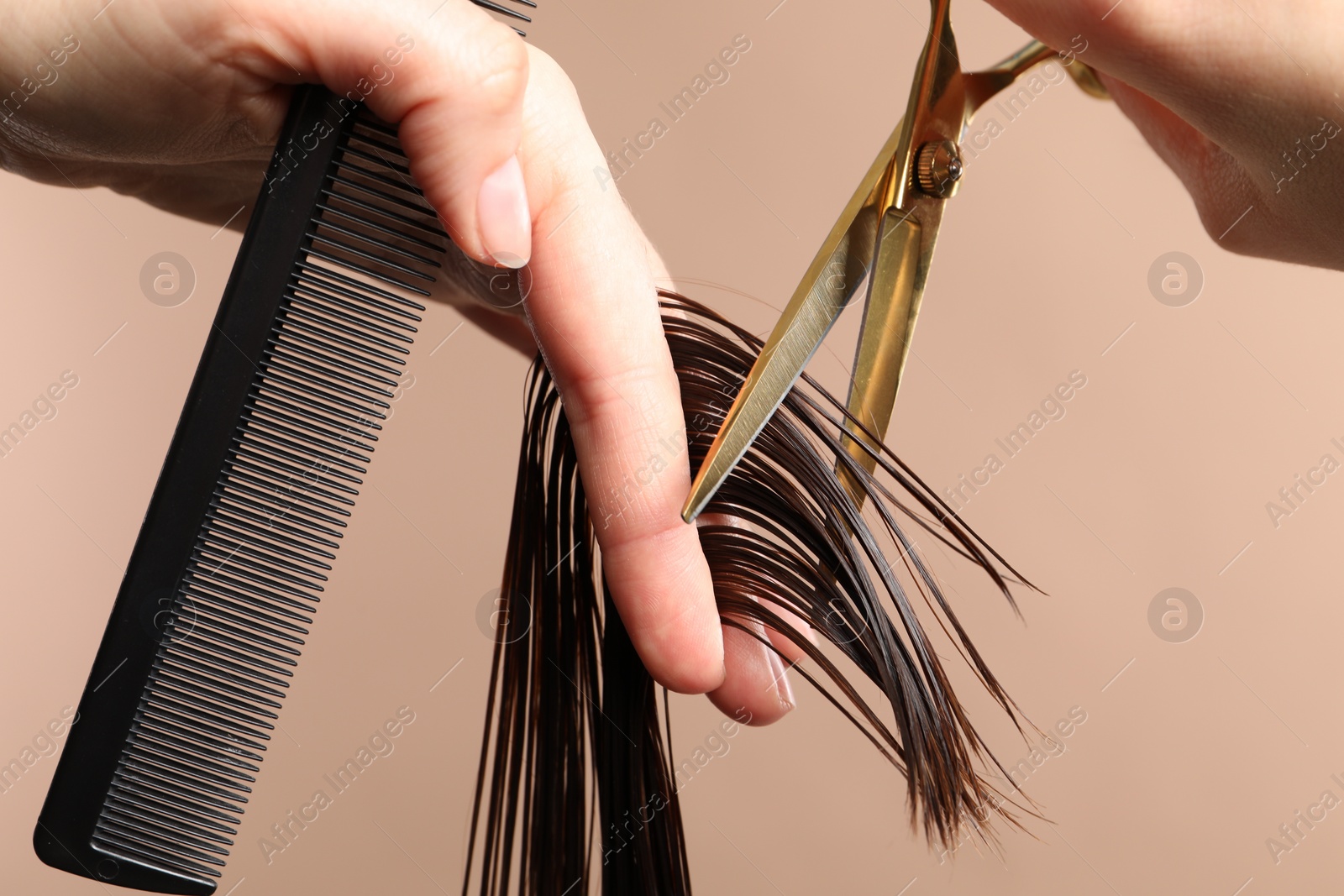 Photo of Hairdresser cutting client's hair with scissors on light brown background, closeup