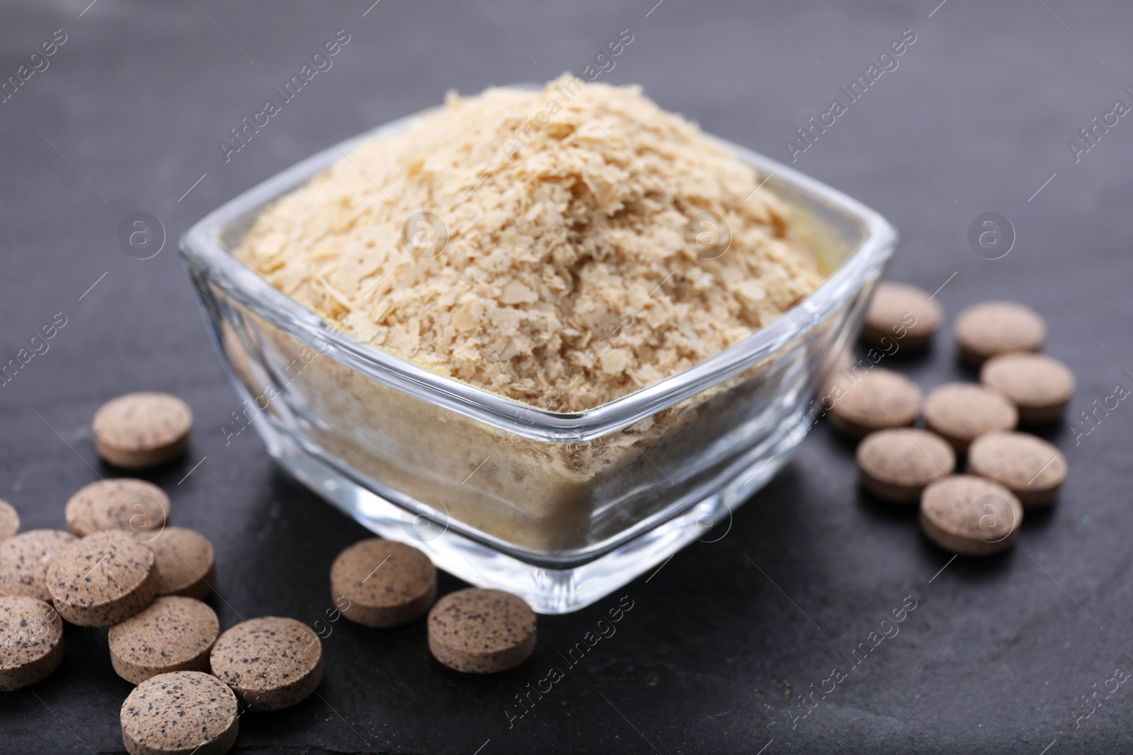 Photo of Brewer's yeast flakes and tablets on black table, closeup