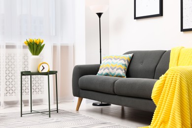 Photo of Spring atmosphere. Stylish living room interior with comfortable furniture and bouquet of beautiful yellow tulips