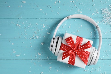 Photo of Modern headphones and gift box on blue wooden background, top view with space for text. Christmas music concept