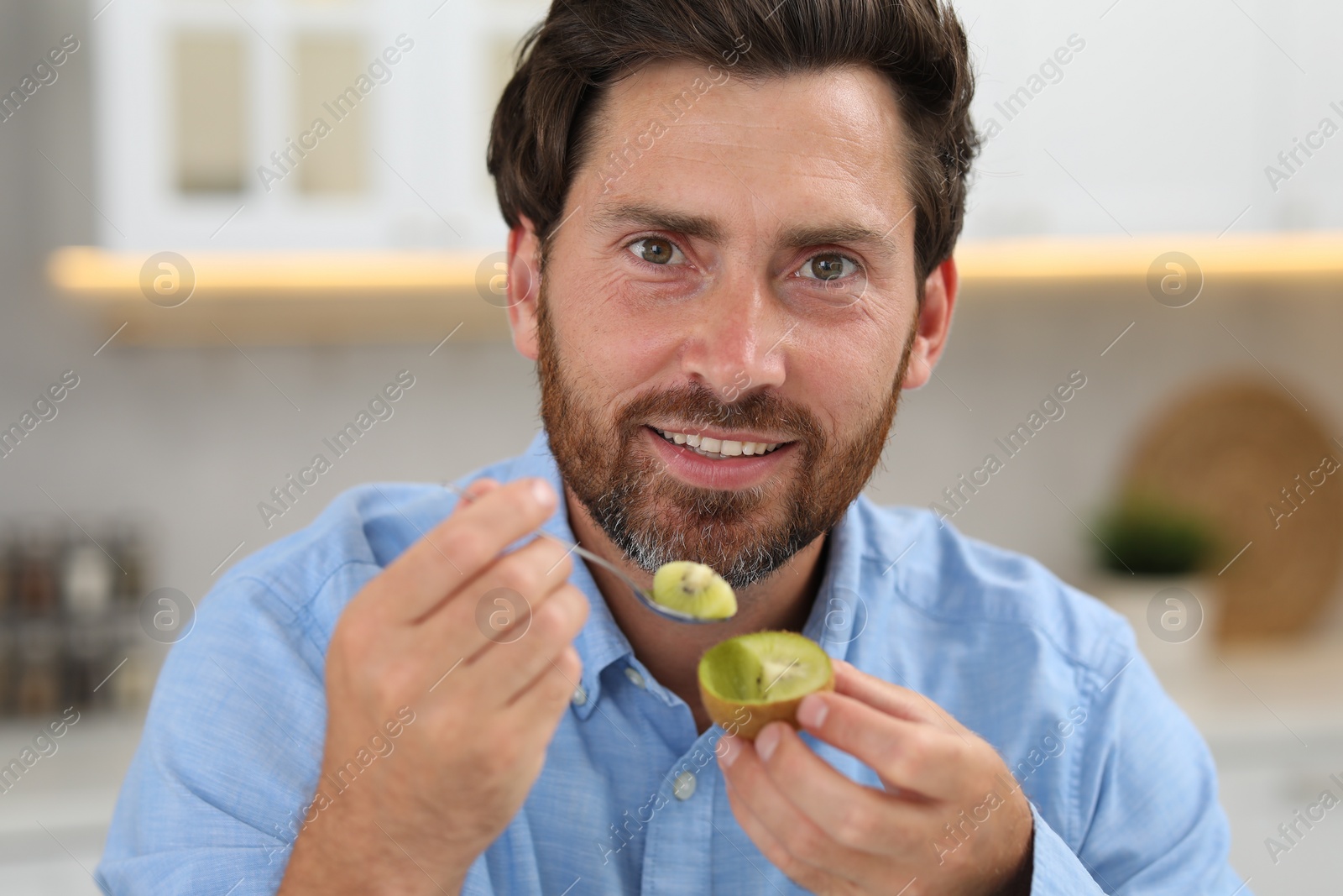 Photo of Man eating fresh kiwi with spoon indoors