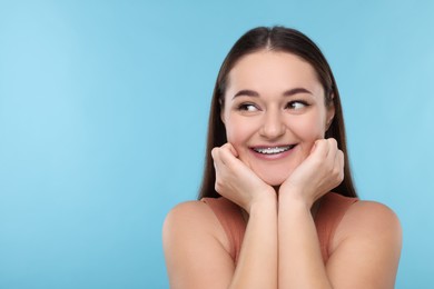 Smiling woman with dental braces on light blue background. Space for text