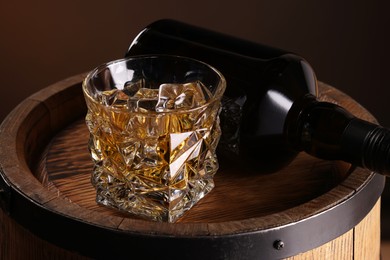 Photo of Whiskey with ice cubes in glass and bottle on wooden barrel, closeup