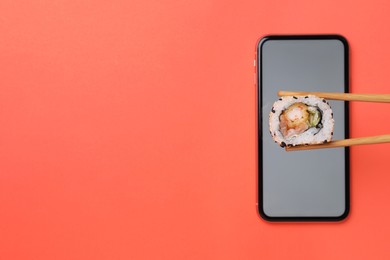 Photo of Holding tasty sushi roll with chopsticks over smartphone on red background, top view. Space for text
