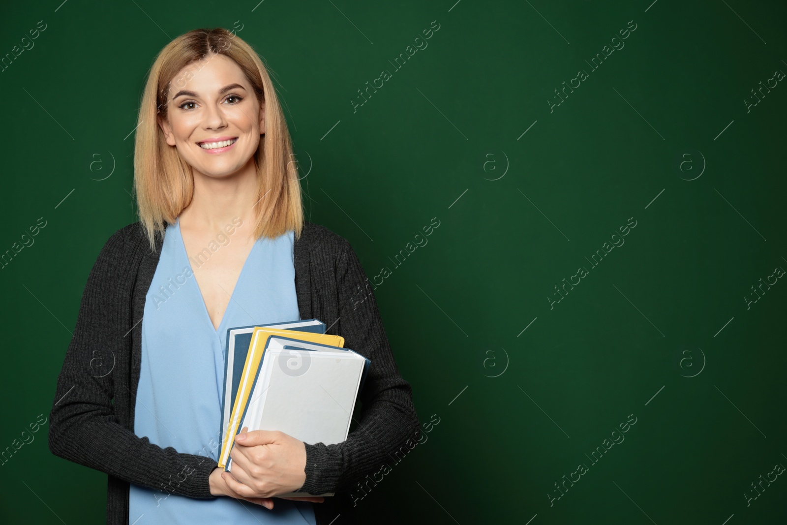 Photo of Portrait of beautiful teacher with books near chalkboard, space for text