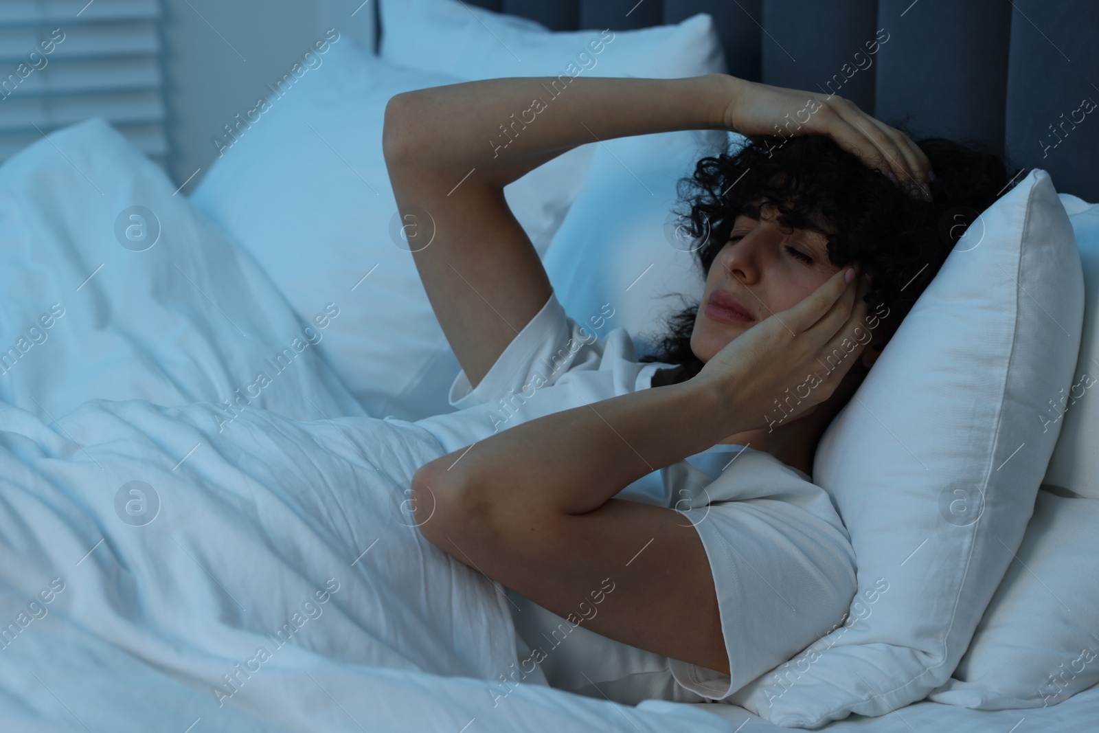 Photo of Young woman suffering from headache in bed at night