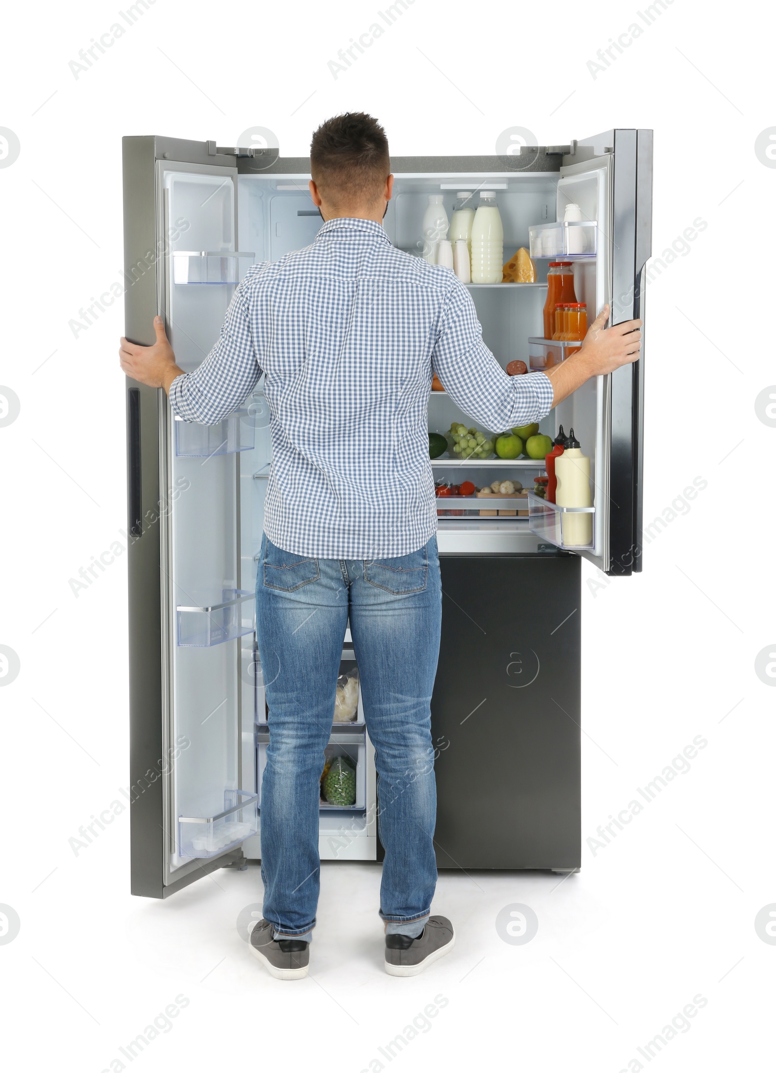 Photo of Young man choosing food from refrigerator on white background