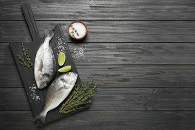 Raw dorada fish on black wooden table, flat lay. Space for text