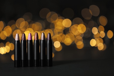 Photo of Set of bright lipsticks on table against blurred lights, space for text