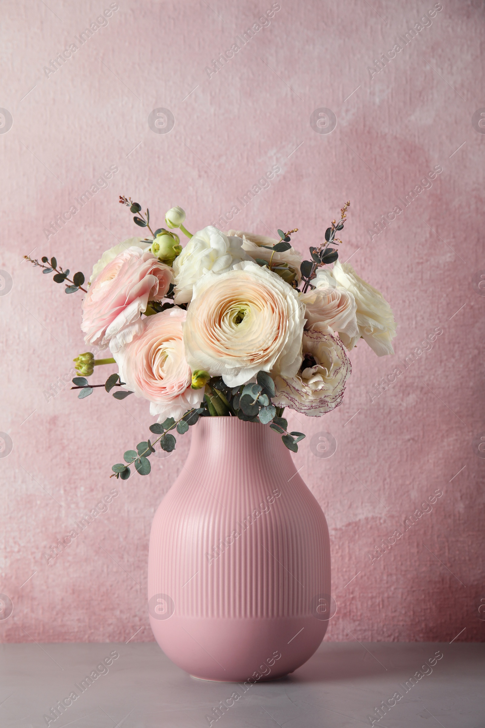 Photo of Vase with beautiful spring ranunculus flowers on table against color background