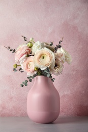 Vase with beautiful spring ranunculus flowers on table against color background