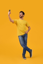 Photo of Smiling man taking selfie with smartphone on yellow background