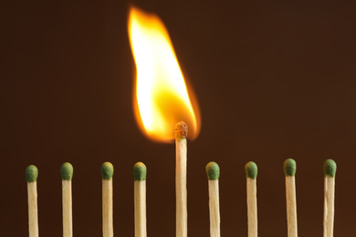 Photo of Burning match among unlit ones on brown background, closeup