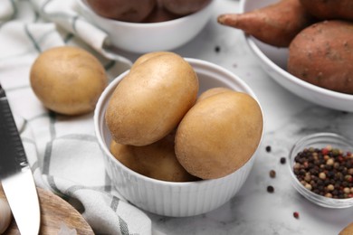 Photo of Different types of fresh potatoes in bowls on white marble table, closeup