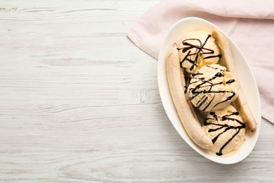 Photo of Delicious banana split ice cream with chocolate topping on white wooden table, top view. Space for text