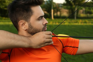 Man with bow and arrow practicing archery in park, closeup